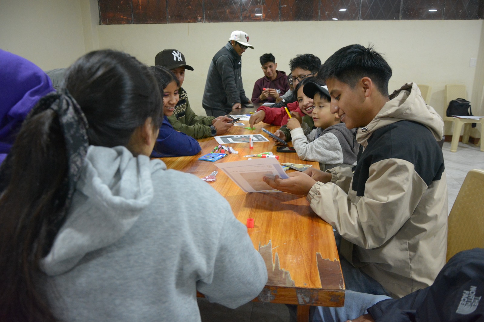 Enhance and upscale this existing photo of a group of people standing indoors at a community workshop in Ecuador, holding handwritten poster boards with their vision and mission statements. Make the image sharper, clearer, and higher resolution in appearance. Increase detail and texture in the clothing, faces, and the handwritten text on the posters. Boost the natural colors — warm indoor light, skin tones, the colorful clothing. Improve overall clarity and sharpness as if it were shot with a high-quality camera. Keep the scene, composition, and all people exactly as they are — do not change or alter any element, just enhance the quality, sharpness, and detail throughout.